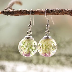 May include: A pair of silver dangle earrings with clear glass orbs containing pressed white and purple flowers.