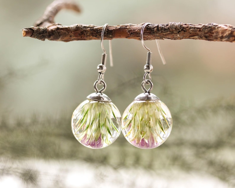 May include: A pair of silver dangle earrings with clear glass orbs containing pressed white and purple flowers.