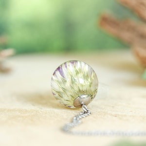 May include: A silver chain necklace with a clear glass pendant containing a pressed flower. The flower is white with purple accents.