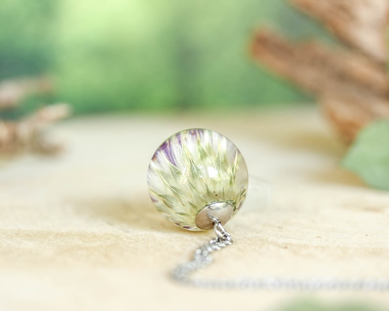May include: A silver chain necklace with a clear glass pendant containing a pressed flower. The flower is white with purple accents.