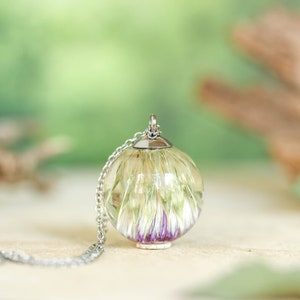 May include: A silver chain necklace with a clear glass pendant containing a dried flower with purple and white petals.