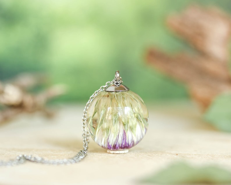 May include: A silver chain necklace with a clear glass pendant containing a dried flower with purple and white petals.
