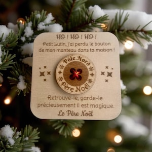 May include: A wooden Christmas ornament with text and a button. The text reads "HO! HO! HO!" and "Père Noël". The button is brown with a red center and the words "Pôle Nord" and "Père Noël" around it. The ornament is decorated with star shapes.