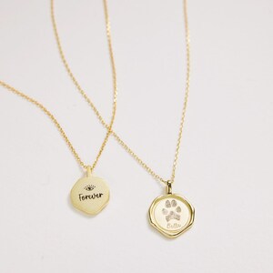 Puede incluir: Dos collares de oro con colgantes. Un colgante tiene la palabra "Forever" y un s&iacute;mbolo de ojo. El otro colgante tiene una huella de pata y la palabra "Bella".