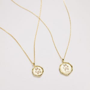 Puede incluir: Dos collares de oro con colgantes de huella de pata. Los colgantes son redondos y tienen un dise&ntilde;o de huella de pata en relieve. Un colgante tiene la palabra "Bella" grabada.