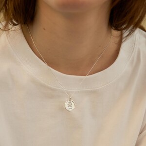 Puede incluir: Un collar de plata con un peque&ntilde;o colgante redondo que presenta una huella de pata. El colgante est&aacute; grabado con la palabra "Aspen".