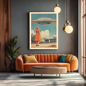 Może przedstawiać: Ilustracja w stylu retro kobiety w jasno pomarańczowej sukience stojącej przed budynkiem, patrzącej w g&oacute;rę na latający spodek. Obraz jest oprawiony i wisi na ścianie nad brązową kanapą z pomarańczowymi poduszkami.