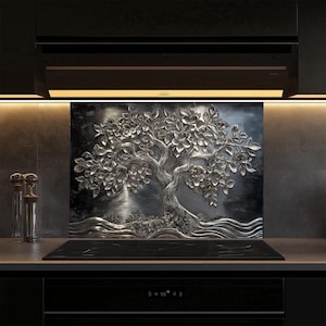 May include: A silver metal backsplash with a 3D embossed design of a tree with flowers. The backsplash is installed above a black stovetop with a black countertop.