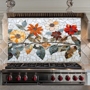 Può includere: Un paraschizzi in mosaico con un design floreale che presenta fiori rossi, arancioni, gialli e marroni con foglie verdi su uno sfondo bianco. Il paraschizzi è installato sopra un fornello in acciaio inossidabile con manopole rosse.