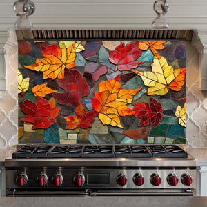 Può includere: Un rivestimento da cucina in mosaico colorato con un design di foglie autunnali in tonalità di rosso, arancione e giallo. Le foglie sono fatte di piccoli pezzi irregolari di vetro e sono disposte in uno schema casuale. Il rivestimento è installato sopra un fornello in acciaio inossidabile con manopole rosse.