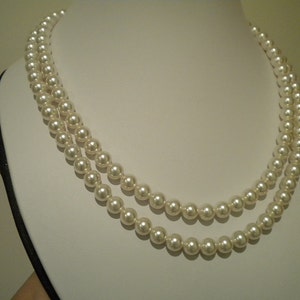 May include: A double strand of white pearl necklace on a white display stand.