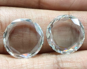 Könnte beinhalten: Zwei klare, runde Edelsteine mit facettierten Kanten werden in einer Hand gehalten. Die Edelsteine sind transparent, reflektieren das Licht und wirken brillant. Die Steine sind wahrscheinlich aus Quarz oder einem ähnlichen Material geschnitten.