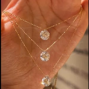 May include: Three-strand gold necklace with round, clear gemstone pendants. The necklaces are layered, with each strand slightly longer than the one above. The gemstones sparkle, and the gold chain is delicate.