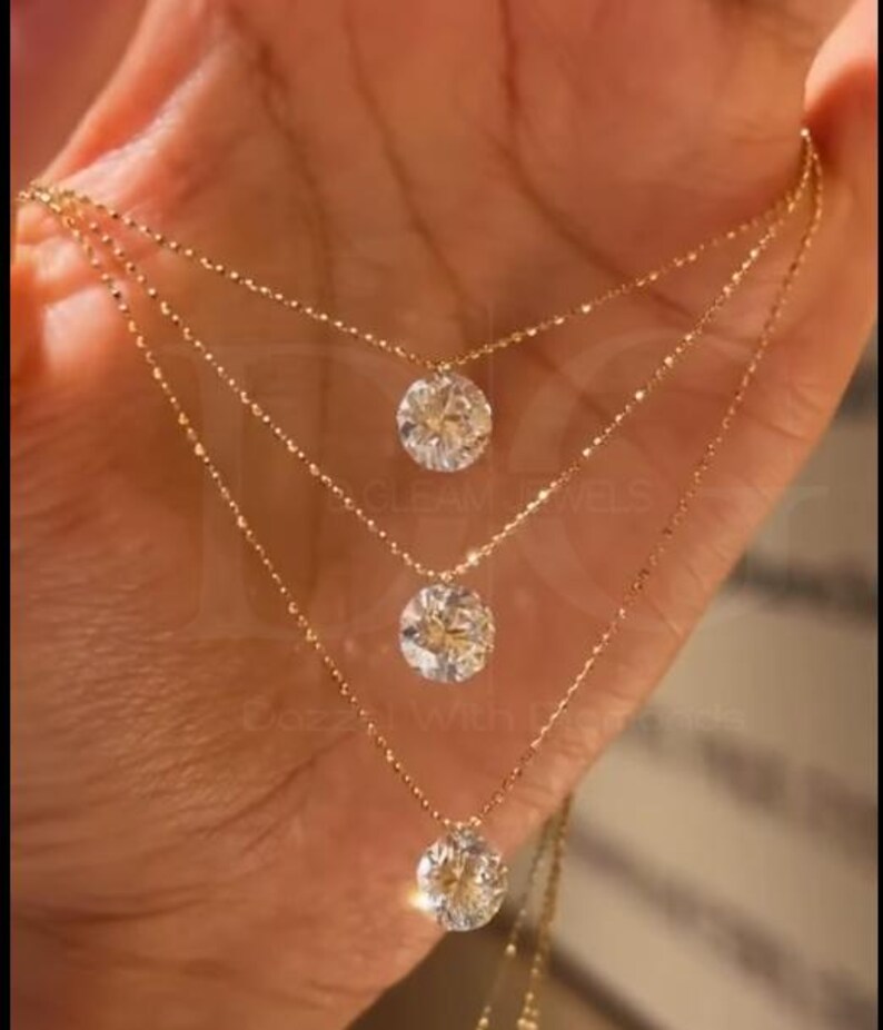 May include: Three-strand gold necklace with round, clear gemstone pendants. The necklaces are layered, with each strand slightly longer than the one above. The gemstones sparkle, and the gold chain is delicate.