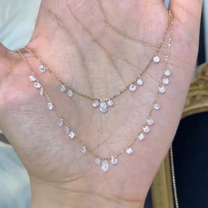 May include: Two delicate gold necklaces with sparkling clear gemstones. The necklaces feature a series of small, round gemstones and larger, teardrop-shaped gems. The necklaces are displayed against a neutral background.