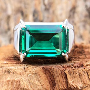 Op de afbeelding: Een zilveren ring met een grote, smaragdgroene edelsteen in een rechthoekige vorm.