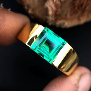 May include: A gold ring with a square emerald green gemstone.