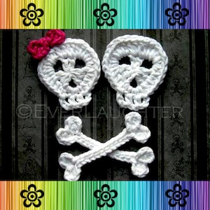 Puede incluir: Dos adornos de calavera de crochet blanco con huesos cruzados, uno con un lazo rosa. Las calaveras tienen ojos negros y una nariz negra.