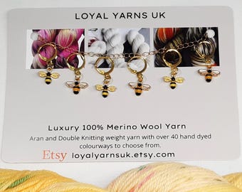May include: A set of six gold-colored stitch markers, each featuring a small bee charm with black and yellow details. The markers are connected by a delicate chain. The card behind the markers reads "LOYAL YARNS UK" and "Luxury 100% Merino Wool Yarn."