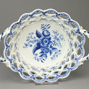 May include: White porcelain basket with a blue floral design. The basket has a lattice design around the rim and handles with a twisted rope appearance. The center of the basket features a blue floral bouquet.