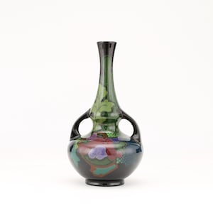 May include: A black ceramic vase with two handles and a green, black, and purple floral design.