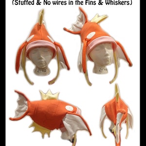 May include: A plush Magikarp Pokemon hat in orange and white. The hat is shaped like a Magikarp with fins and a tail. The hat is stuffed and has no wires in the fins or whiskers. The text "Pokemon - Magikarp (Stuffed & No wires in the Fins & Whiskers)" is written above the hat.