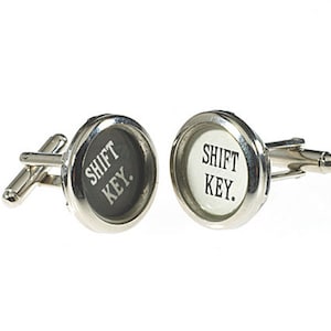 May include: A pair of silver cufflinks with black and white round inserts. The inserts feature the text "SHIFT KEY."