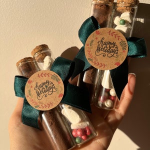 Pu&ograve; includere: Due provette di vetro riempite con polvere di cacao, marshmallow e caramelle rosse e verdi. Le provette sono legate con un nastro verde e un'etichetta di carta marrone che dice "Buone Feste".