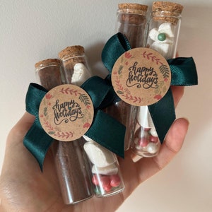 Pu&ograve; includere: Tre provette di vetro riempite con miscela per cioccolata calda, marshmallow e codette rosse e bianche. Ogni provetta &egrave; sormontata da un tappo di sughero e legata con un nastro verde e un'etichetta di carta marrone su cui &egrave; scritto "Buone Feste".