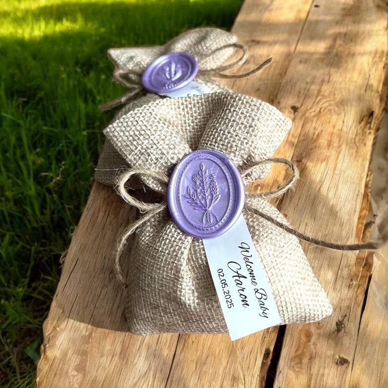 May include: Two small burlap bags with purple wax seals and a lavender design. The bags have a white tag that says "Welcome Baby  Harron 02.05.2025".