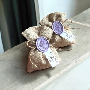 May include: Two small burlap bags with lavender-colored wax seals and personalized tags. The tags read "Welcome Baby Sophie 03.05.2025" and "Welcome Baby Aaron 02.08.2025".
