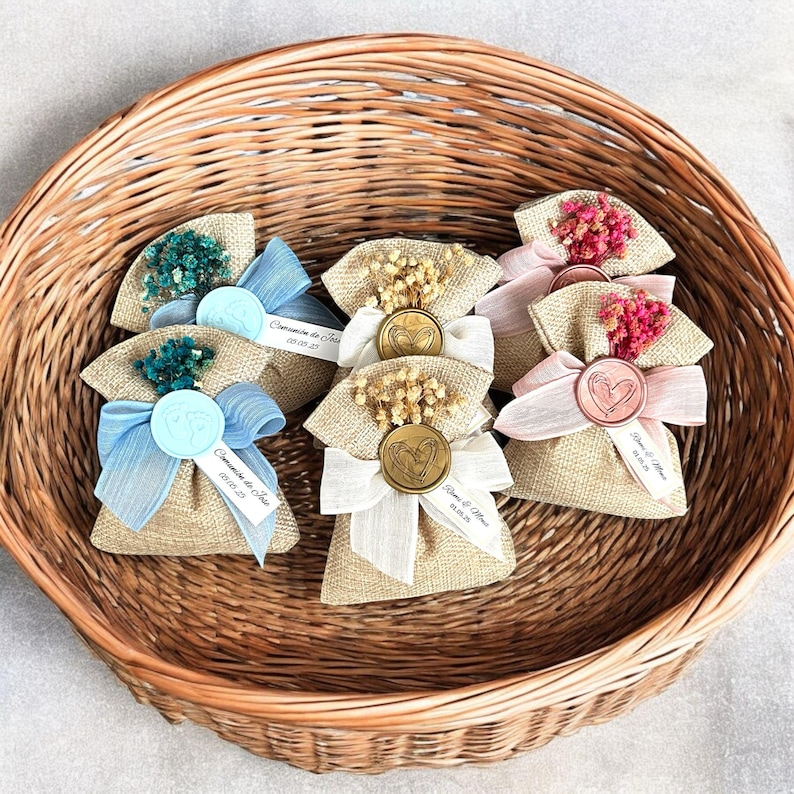 May include: A wicker basket filled with small burlap bags tied with ribbon and decorated with dried flowers. Each bag has a wax seal with a heart design and a personalized tag with the text "Comuni&oacute;n de Sof&iacute;a 05.05.23" or "David & Alma 05.05.23".