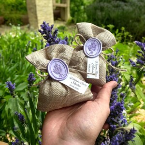 May include: Two small burlap bags with lavender-scented sachets. Each bag has a wax seal with a lavender sprig design and a personalized tag with the text "Welcome Baby Sophie 02.05.2023" and "Welcome Baby  Arianna 02.05.2023".