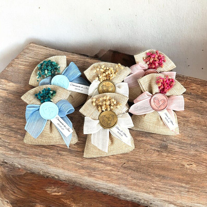 May include: Assortment of small burlap bags with different colored ribbons and dried flowers. Each bag has a wax seal with a heart design and a personalized tag with a name and date.