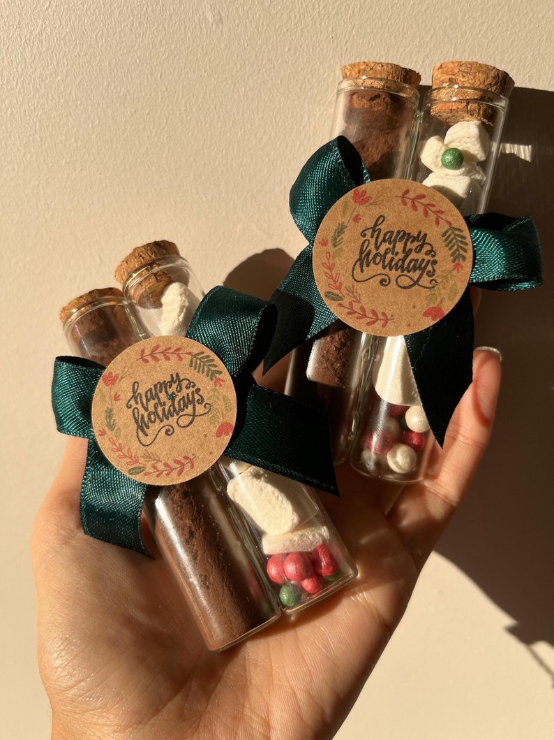Pu&ograve; includere: Due provette di vetro riempite con polvere di cacao, marshmallow e caramelle rosse e verdi. Le provette sono legate con un nastro verde e un'etichetta di carta marrone che dice "Buone Feste".