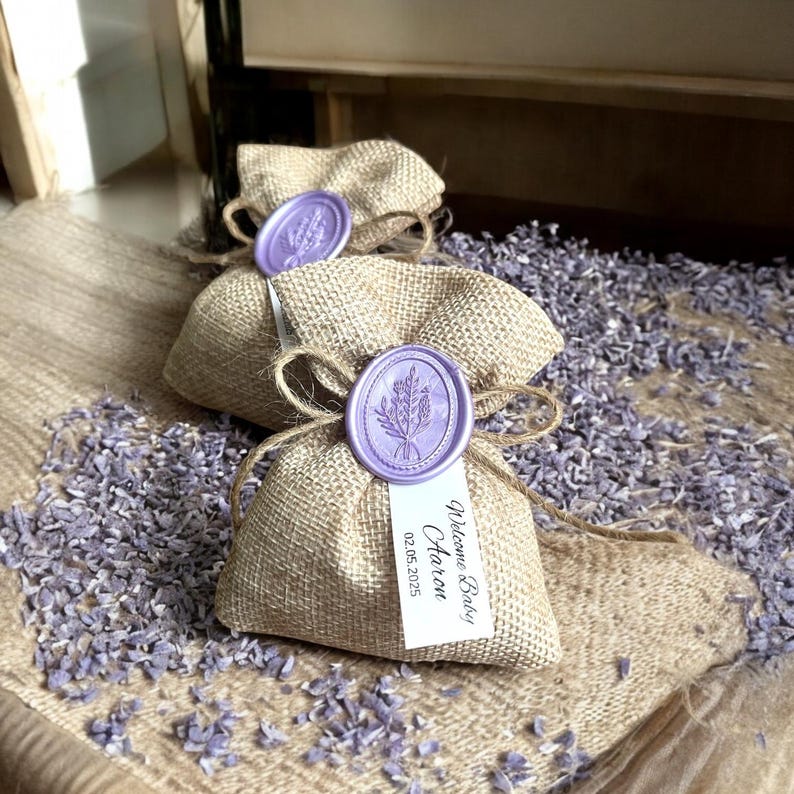 May include: Three small burlap bags with lavender inside. Each bag has a purple wax seal with a lavender sprig design. One bag has a white tag that says "Welcome Baby Aaron 02.05.2025".