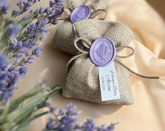 Puede incluir: Dos pequeñas bolsas de arpillera con saquitos perfumados con lavanda. Cada bolsa tiene un sello de cera púrpura con un diseño de rama de lavanda. Una bolsa tiene una etiqueta blanca con el texto "Bienvenido Bebé Aaron 02.05.2025".
