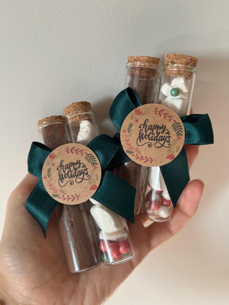 Pu&ograve; includere: Tre provette di vetro riempite con miscela per cioccolata calda, marshmallow e codette rosse e bianche. Ogni provetta &egrave; sormontata da un tappo di sughero e legata con un nastro verde e un'etichetta di carta marrone su cui &egrave; scritto "Buone Feste".
