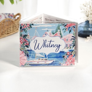 Beach and sailboat themed personalized coastal mahjong card cover featuring a sailboat harbor scene in blue and pink colors, waterfront cottage, floral accents, and optional clear sleeve for Large NMJL cards