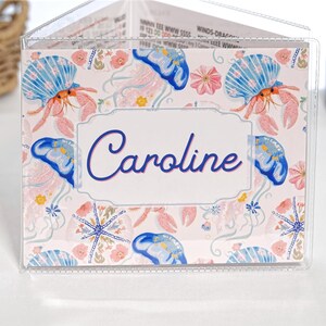 Pretty Jellyfish personalized mahjong card cover for Large NMJL cards, shown in a clear sleeve with the name Caroline, featuring pastel beach ocean artwork with blue jellyfish, pink coral, seashells, starfish, flowers, aqua, coral, blush, navy, and soft coastal colors as a custom mahjong card holder and Mah Jongg accessory.