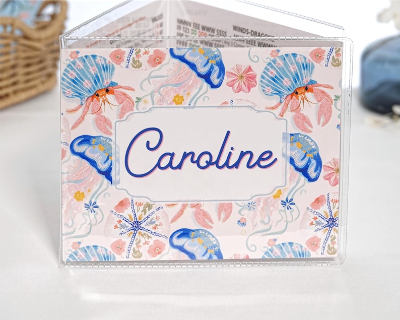 Pretty Jellyfish personalized mahjong card cover for Large NMJL cards, shown in a clear sleeve with the name Caroline, featuring pastel beach ocean artwork with blue jellyfish, pink coral, seashells, starfish, flowers, aqua, coral, blush, navy, and soft coastal colors as a custom mahjong card holder and Mah Jongg accessory.