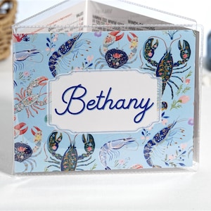 Blue Shellfish personalized mahjong card cover for Large NMJL cards, shown in a clear sleeve with the name Bethany, featuring detailed ocean beach coastal artwork with light blue, navy, coral, pink, shrimp, crab, lobster, and shellfish motifs as a custom mahjong card holder and Mah Jongg accessory.