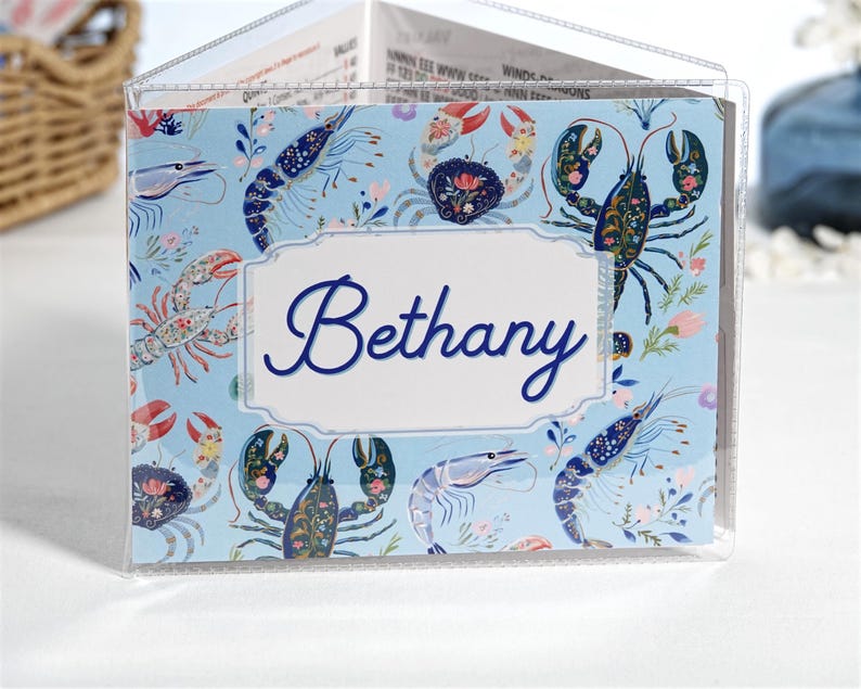 Blue Shellfish personalized mahjong card cover for Large NMJL cards, shown in a clear sleeve with the name Bethany, featuring detailed ocean beach coastal artwork with light blue, navy, coral, pink, shrimp, crab, lobster, and shellfish motifs as a custom mahjong card holder and Mah Jongg accessory.