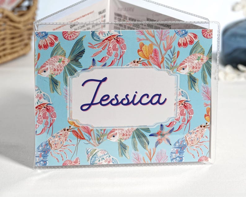 Tropical Reef personalized mahjong card cover for Large NMJL cards, shown in a clear sleeve with the name Jessica, featuring bright ocean beach coastal artwork with aqua blue, coral pink, tropical fish, shrimp, shells, sea plants, starfish, and reef details as a custom mahjong card holder and Mah Jongg accessory.