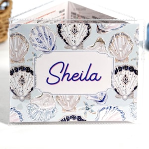 Pearl Shells personalized mahjong card cover for Large NMJL cards, shown in a clear sleeve with the name Sheila, featuring ocean beach coastal seashell artwork in soft blue, cream, navy, gold, pearl, and blush tones as a custom mahjong card holder and Mah Jongg accessory.