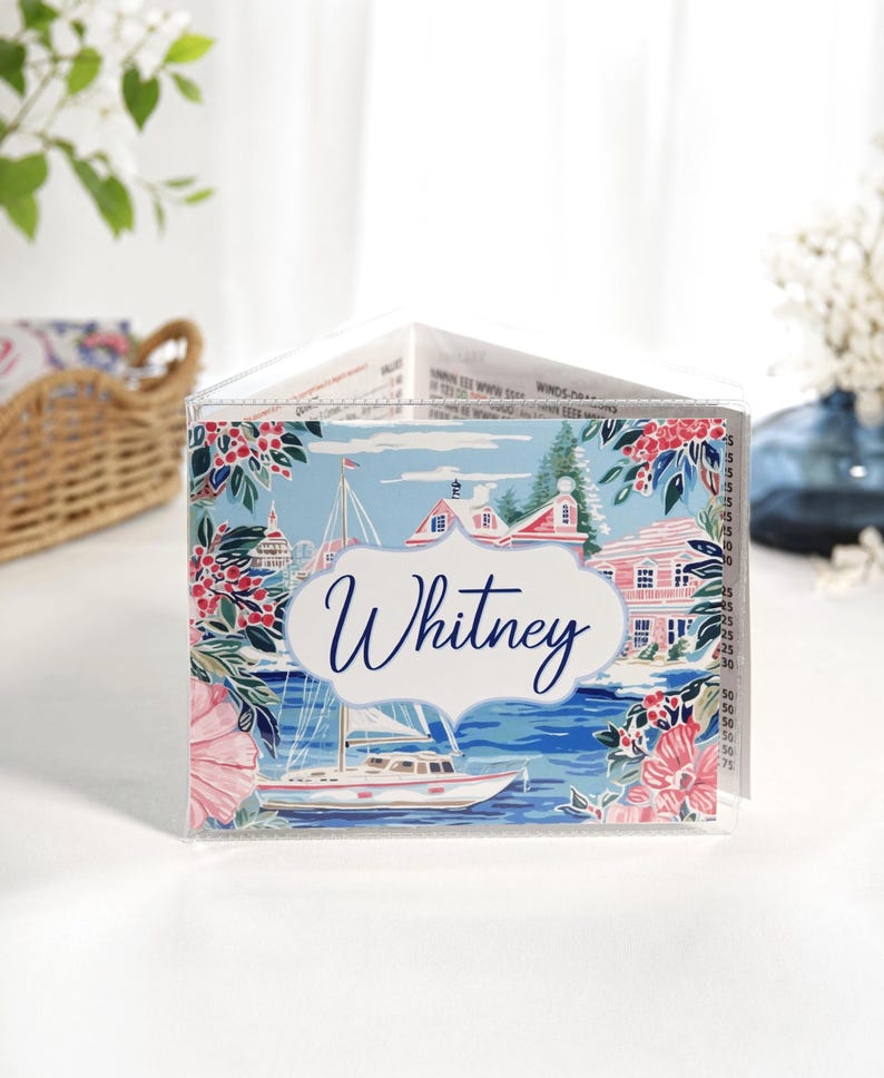 Beach and sailboat themed personalized coastal mahjong card cover featuring a sailboat harbor scene in blue and pink colors, waterfront cottage, floral accents, and optional clear sleeve for Large NMJL cards