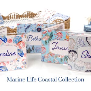 Marine Life Coastal Collection personalized mahjong card covers for Large NMJL cards, featuring ocean beach coastal designs in pastel blue, pink, coral, and aqua, including jellyfish, shellfish, tropical reef, and pearl shells shown in clear protective sleeves.