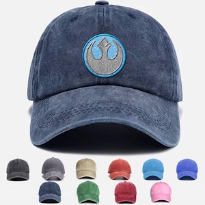May include: A distressed navy blue baseball cap with an embroidered emblem in blue and grey. The cap has a curved peak and a fabric strap. Several other caps in different colours are shown below.