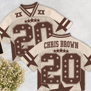 Pu&ograve; includere: Due maglie da football americane beige e marroni con il nome "CHRIS BROWN" e il numero "20" sul retro. Le maglie hanno dettagli a stella e il numero "XX" sulle spalle. Le maglie sono in rete e hanno strisce marroni sulle maniche.