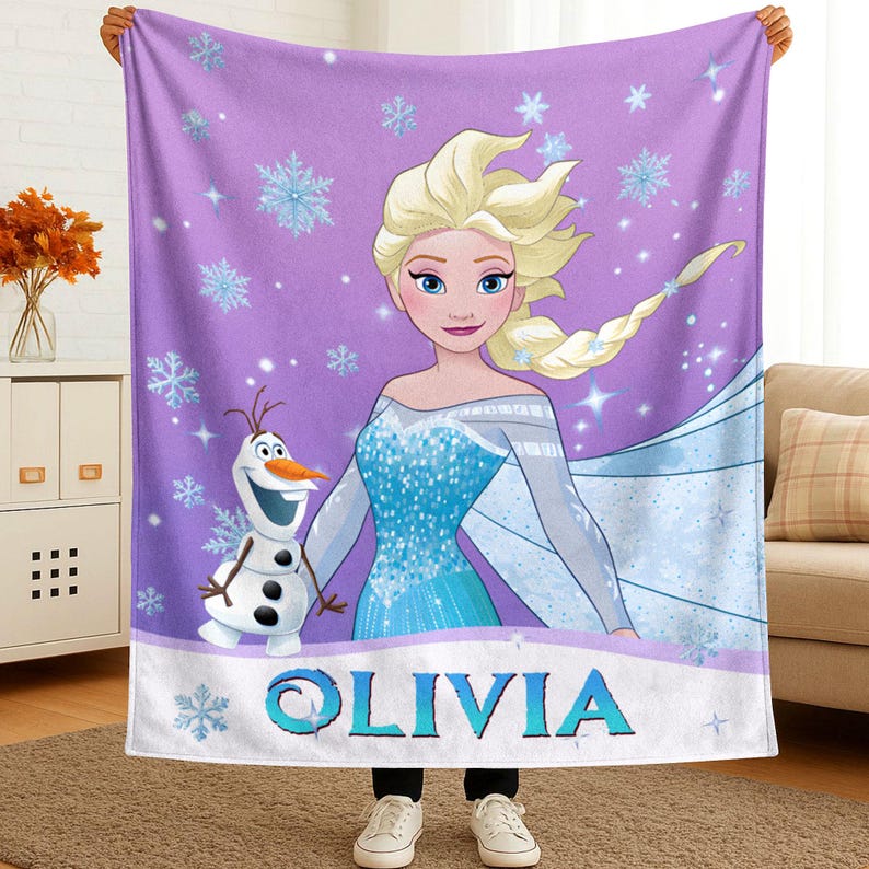 May include: A purple fleece blanket featuring a graphic of a blonde character in a blue dress and a snowman character. The background is decorated with light blue snowflakes and sparkles. The name OLIVIA is printed in large blue letters at the bottom.